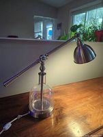Lamp fully assembled on wooden surface showing brushed aluminum arm, joints, dome shade, and glass base.