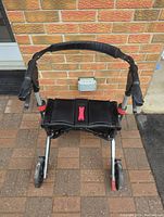 Front view showing the padded handle grips, seat, and front wheels of the collapsible walker.