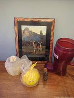 Full view of five items: framed deer picture, yellow smiley candle wrapped in plastic, selenite candle holder, small wood carving, large red glass boot