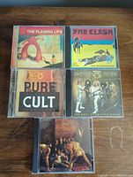 Front view of five CD albums showing cover art for The Flaming Lips, The Clash, The Cult, Twisted Sister, and Skid Row.
