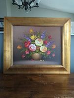 Full front view of the framed flower still life painting with gold frame on a wooden surface.