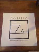 Front cover of Frank Zappa album 'Ship Arriving Too Late to Save a Drowning Witch' showing minimalist design with geometric shapes and album title.