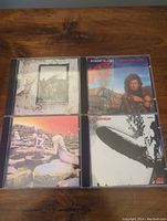 Four Led Zeppelin CD albums laid out on a wood surface showing front covers: Houses of the Holy, Now and Zen, Led Zeppelin, Robert Plant.