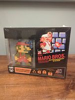 Front view of factory sealed Nintendo Super Mario Bros. Entertainment System collector's box with pixelated Mario figurine visible through display window, shrink wrap intact.
