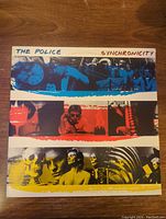 Front cover of The Police 'Synchronicity' vinyl album showing colorful horizontal photo strips with band imagery and artwork.