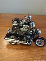 Three miniature motorcycles lined up on a wooden surface showing detailed chrome and black Harley Davidson and Victory models