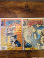 Two Black Cat Marvel comics laid side by side, protected in sleeves with backing boards. Comics feature vivid cover art showing Black Cat in action.