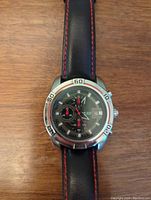 Front view of Megir wristwatch showing black dial with chronograph, date window, and black leather strap with red stitching.