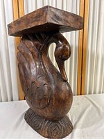 Full side view of the carved wooden swan stand showing the flat top, swan body, and base with swirl carving detail.