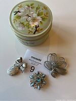 Four items in the lot including three silver-toned brooches and a Sadler jar with apple blossom decoration