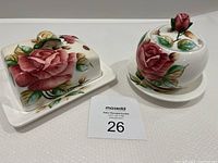 Butter dish with lid and jam/honey pot both featuring hand-painted rose patterns, placed on white surface with auction lot number.