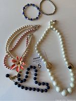 Photo showing multiple costume jewelry pieces including three necklaces, two bracelets, and part of a ring, arranged on white surface