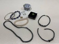 Photo showing variety of costume jewelry including necklaces, bracelets, ring, and pendant in blue, black, silver and pearl tones