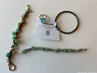 Photo showing three bracelets and one ring arranged on a white surface with auction tag