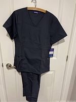 Full view of gray scrub set hanging, showing top and pants together with tags.