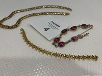 Lot showing three vintage ladies jewelry pieces: Sarah Coventry rainbow glass bracelet, Premier Designs wide gold-tone Byzantine necklace, and Premier Designs gold-tone cross and XO bracelets.