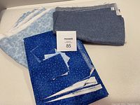 Lot consisting of various blue tone quilting fabrics folded and stacked with small cut squares on top, showing different shades and patterns of fabric.