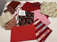 Variety of folded quilting fabric squares in various red tones with assorted patterns including florals, stars, geometric prints, and script lettering.