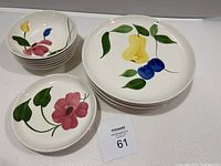 Photo showing stacked 6 small bowls with floral designs, 5 small plates with pink flower design, and 6 dinner plates with yellow, blue, and pink handpainted fruit/flower designs.