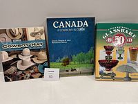 Three hardcover coffee table books stacked vertically: The Cowboy Hat Book, Canada A Symphony in Color, and Collectible Glassware 40 50 60s.