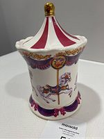 Porcelain cookie jar with carousel design featuring a red and white striped roof and painted carousel horses with floral and gold detailing.