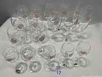 Full set of vintage Bohemian crystal stemware with pink rose and gray leaf motif, multiple glasses arranged on white surface.