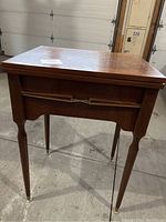 Side angle view of the wooden sewing table showing slender tapered legs and closed hinged top lid.