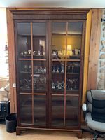 Front view showing two glass-front doors with wooden mullions and interior shelves filled with glassware and collectibles.