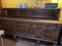 Full frontal view of antique wooden sideboard showing 3 drawers and 4 doors, carved pineapples on legs.