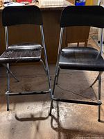 Front view of two black IKEA Franklin foldable bar stools with backrest showing the black wooden seats and metal frames.