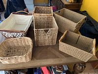Seven assorted wicker and sea grass baskets arranged on a wooden table.