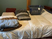 Photo showing full box down duvet on bed with two duvet covers folded on top, microfibre throws on top, and grey Rubbermaid laundry basket on feather bed.