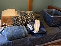Electric warming throw with four fleece throws and four pillows arranged on a bed; includes a black-and-white cat pattern rectangular pillow, solid colored pillows and throws mostly in neutral and blue tones.