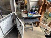 Photo showing two folding plastic tables and Coleman propane stove/grill with BBQ tools and fuel canisters on top.