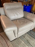 Front and angled view of beige leather electric recliner chair showing padded armrests and backrest with some surface creases and scratches.