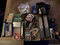 Top-down view of all emergency supplies arranged on a wooden table including binoculars, flashlights, radio, batteries, emergency blankets, and headlamps.