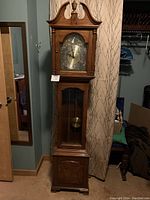 Full view of the grandfather clock showing overall shape, wood finish, and base.
