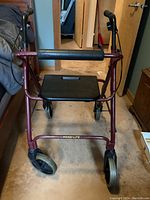 Front-facing view of Handilite walker showing burgundy metal frame, padded bar, black seat, and two front larger wheels.