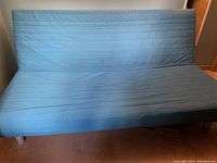 Futon with blue removable cover laid out flat as a bed, visible slightly wrinkled, showing overall condition of the fabric and mattress thickness.