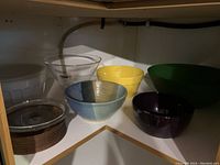 Mixed kitchen bowl assortment on shelf including glass, ceramic, pottery, plastic bowls and wooden plates