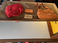 Full length wood-framed mirror, orange canvas purse, red PVC purse with woven detail, small beige and gold wallets placed on a wooden surface.