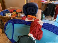 Photo showing various outdoor gear items including pool float, sleeping bag, Canadian flag, and other camping accessories on a chair and table.