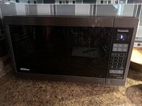 Front view of Panasonic microwave oven showing black door with reflective glass and control panel to right.