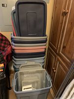 Stack of Rubbermaid totes with lids in various colors and sizes in corner of room.