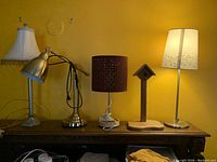 Front view of four assorted table lamps arranged on a shelf with a wooden bird perch ornament between two lamps