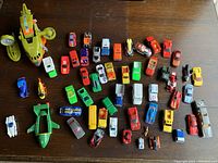 Top view of the entire lot showing a large green and yellow spacecraft toy and about 38 vintage metal cars of various colors and types scattered on a brown surface.