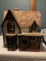 Front view of the Victorian-style wooden dollhouse showing the pitched roof with wooden shingles, green trim, and bay window detail on the front.