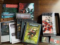 Top view of 6 Warhammer 40,000 books stacked with pack of cards and accessories beside them