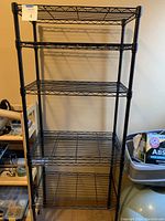 Black wire shelving unit with six shelves against a wall, measuring approximately 23 x 13 x 60 inches.