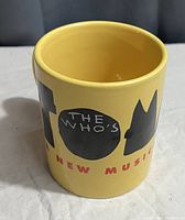 Photo of yellow ceramic mug showing 'The Who's' text with musical reference on one side